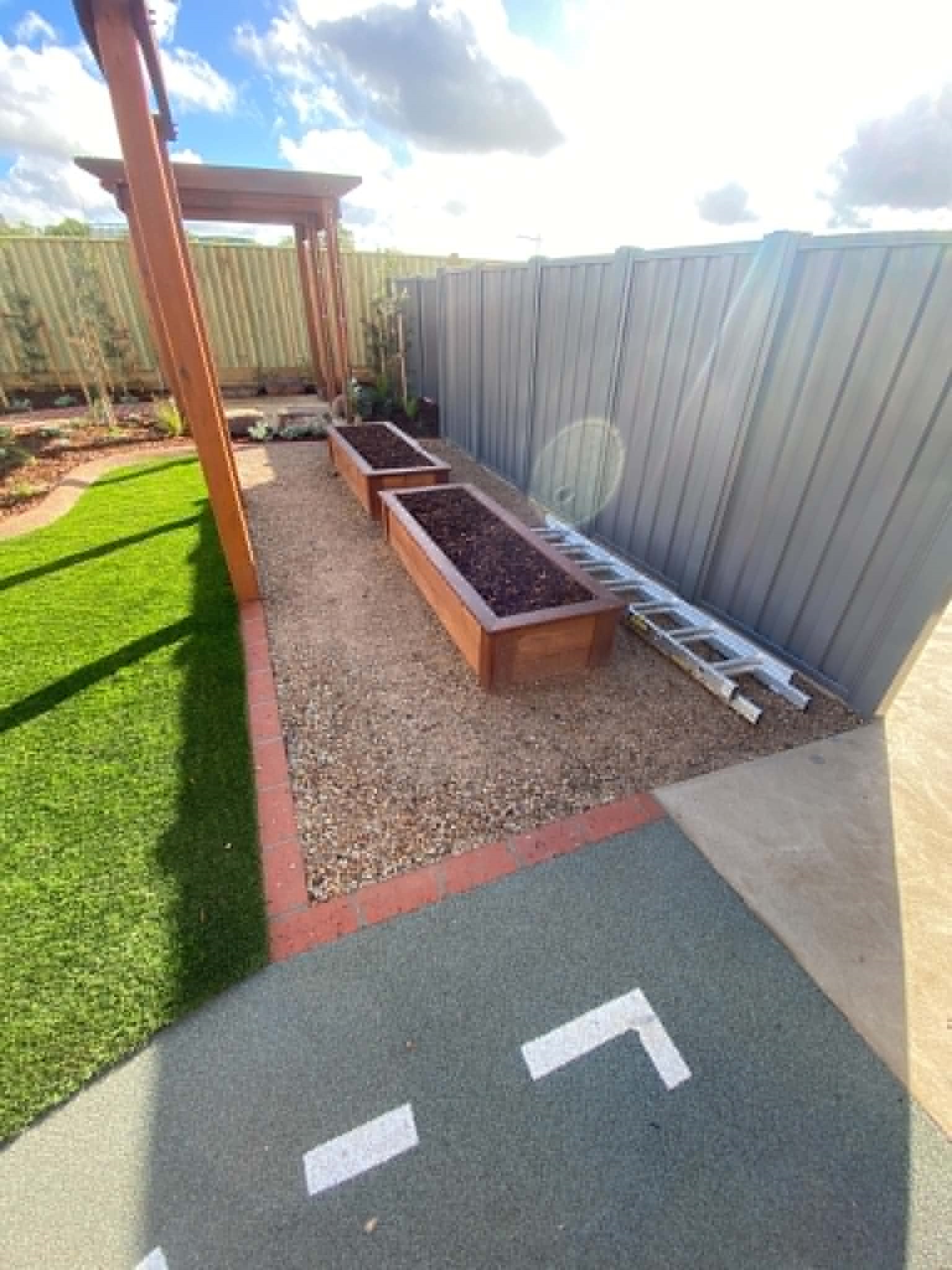 A functional childcare outdoor learning area with raised garden beds, gravel pathways, synthetic turf, and roadway-style soft-fall surfacing designed for safe play and hands-on exploration.
